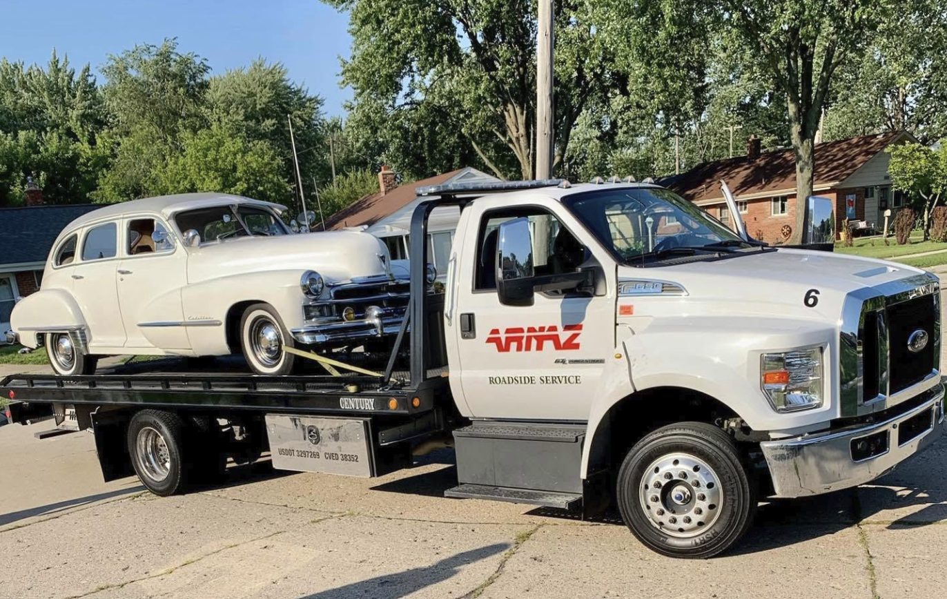 White ARNAZ flatbed tow truck carrying a classic car